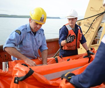 Crew in safety gear handling a life raft during a supply operation